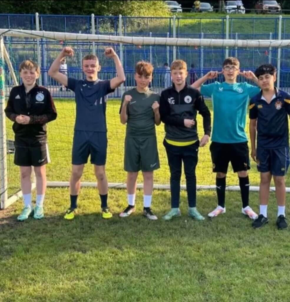 Six young boys in sports kit cheering in a football goal